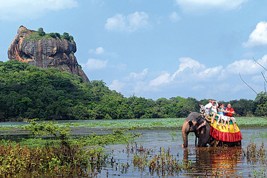 Tourists take an elephant ride in the shadow of the ancient Sigiriya rock fortress