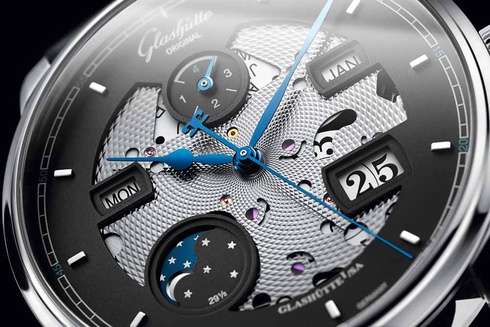 The matte grey dial has been partially opened in the centre and around the indications to reveal the main plate of the perpetual calendar module
