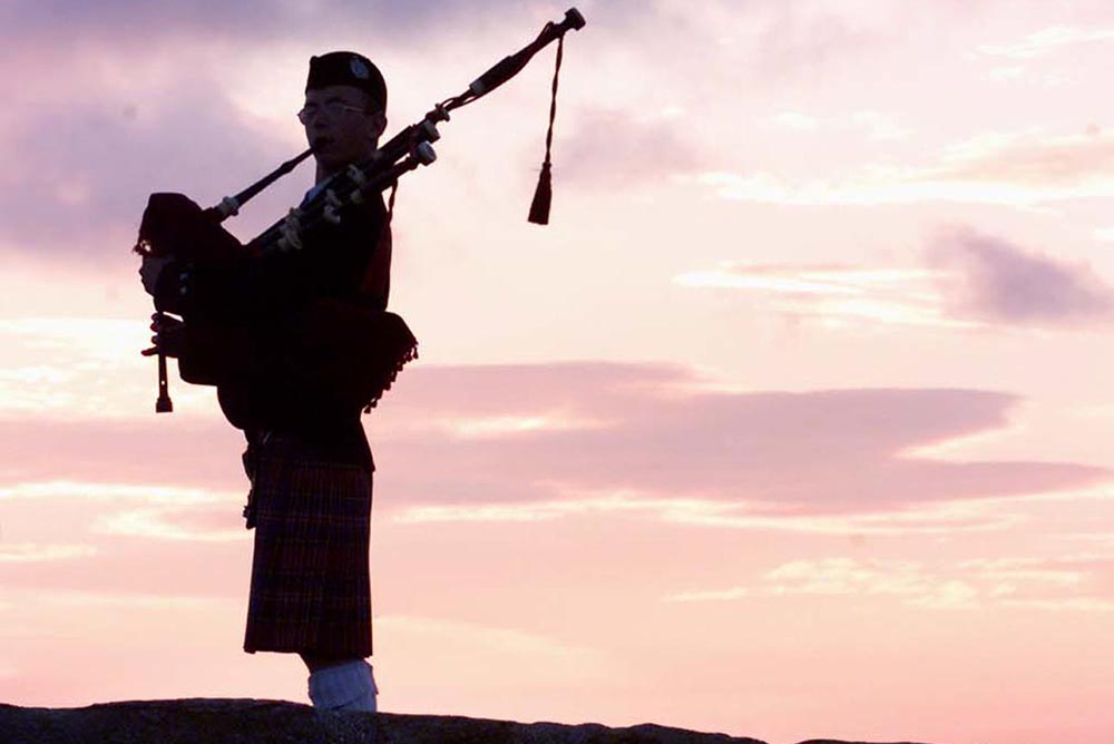 A bagpiper plays on the bridge over Swilken Burn